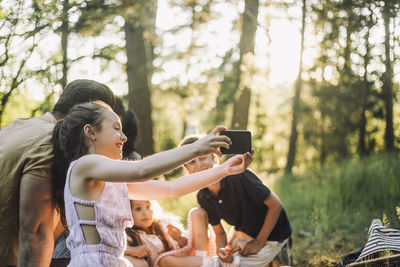 Girl taking selfie with father through smart phone during picnic in forest