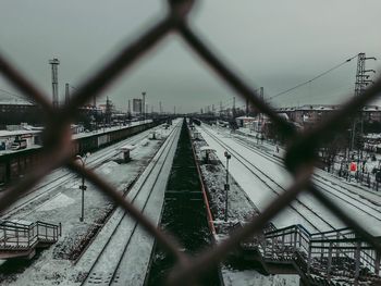 Train on railroad track against sky seen through chainlink fence