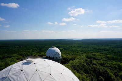 Scenic view of green forest, white radio station against sky