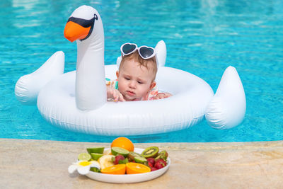 Baby in inflatable ring looking at plate of fruits
