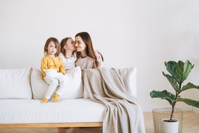 Young happy family woman mother with two children girls on couch in living room at home