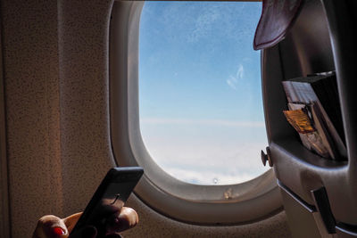 Cropped hand holding mobile phone by window in airplane