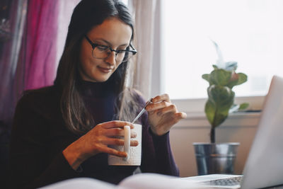 Young woman holding coffee cup with laptop and book on table in college dorm