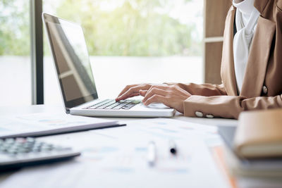 Midsection of businesswoman using laptop at desk in office