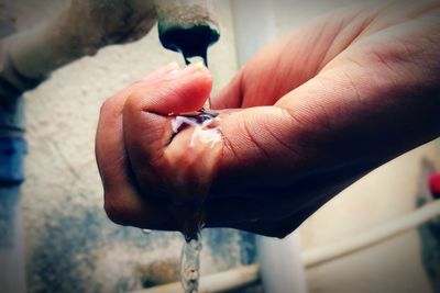 Water from faucet pouring in cropped hand