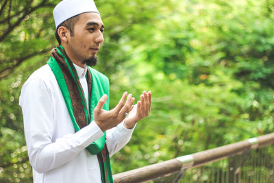 Mid adult man praying while standing by railing at park