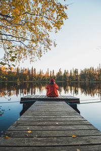 Girl sits at the end of a wooden pier looking out into water  in sotkamo, kainuu region, finland.