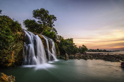 Scenic view of waterfall in forest against sky