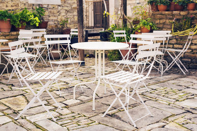 Empty chairs and tables at sidewalk cafe amidst buildings