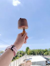 Midsection of person holding ice cream against sky