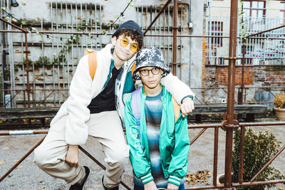 Portrait of boy arm around with male friend while sitting on railing