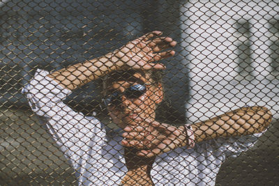 Portrait of woman wearing sunglasses standing by chainlink fence