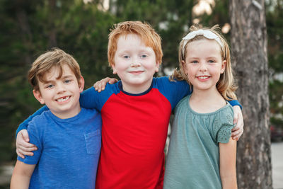 Three happy caucasian little children kids boys and girl hugging together outdoor in park. 