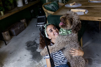 Smiling woman with dog taking selfie at home