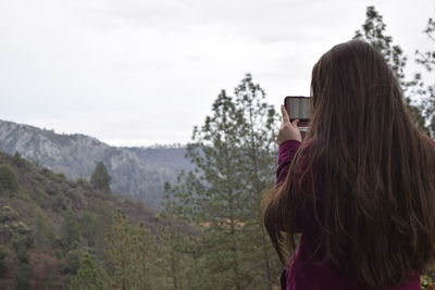 Rear view of woman photographing mountains through mobile phone