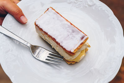 High angle view of hand holding mille-feuille in plate outdoors