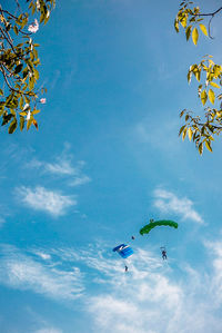 Low angle view of people paragliding against sky