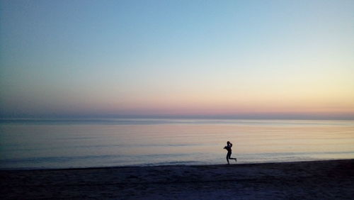 Silhouette man on beach against clear sky during sunset