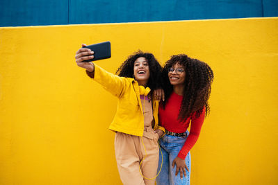 Female friends taking selfie against yellow wall