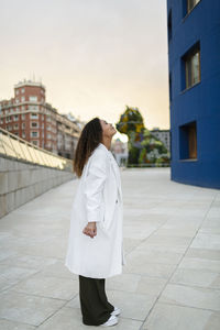 Young woman wearing overcoat while standing on footpath during sunset