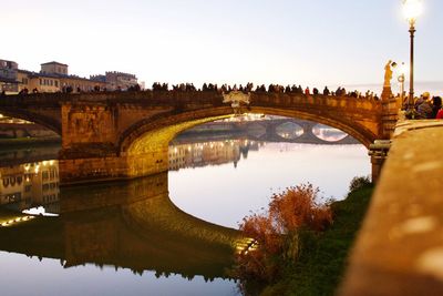 Arch bridge over river amidst buildings against sky