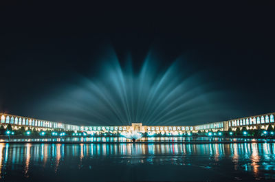 Illuminated bridge over river against sky at night