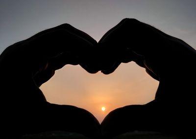 Silhouette hand holding heart shape against sky during sunset