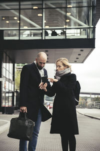 Businesswoman showing smart phone to businessman on city street