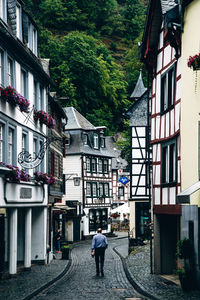 Rear view of man walking on street amidst buildings