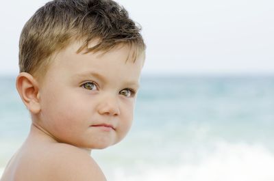 Close-up of shirtless baby boy looking away against sea