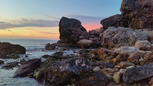 Rocks on sea shore against sky during sunset