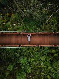 Aerial view of woman sitting on footbridge in forest