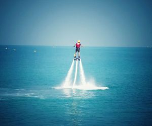 Rear view of person flyboarding at sea against blue sky