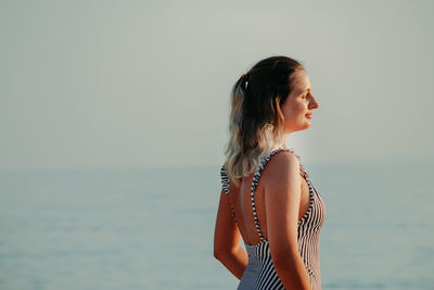 Side view of young woman standing in sea against sky