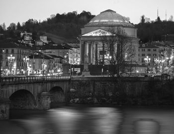 Arch bridge over river by buildings against sky in city. night dark black and white photo 