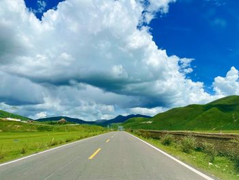 Empty road along landscape against cloudy sky