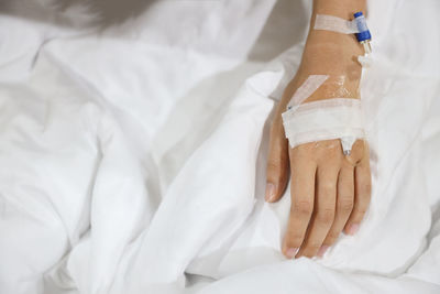 Cropped hand of woman with iv drip relaxing on bed at hospital