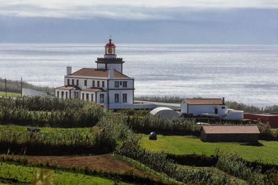 Lighthouse amidst sea and buildings against sky