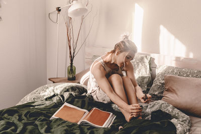 Young woman sitting on bed at home