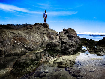 People standing on rock by sea against sky