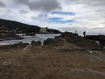 People walking on beach against cloudy sky