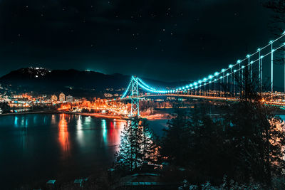 Illuminated bridge over river in city at night