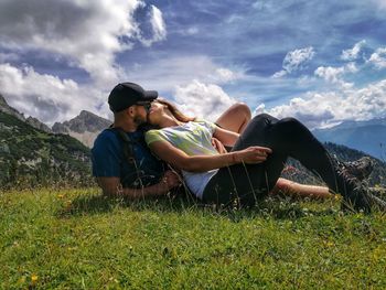 Lovers sitting on field against sky