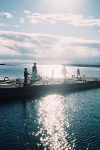 Silhouette people on dock on sea