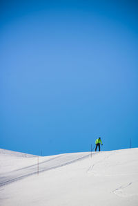 Man walking on snow covered land against clear blue sky