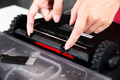 Close-up of a young caucasian woman's hands servicing the brush compartment of a robot vacuum