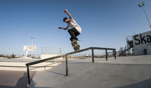 Low section of man skateboarding on skateboard against clear sky