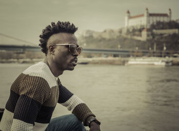 Side view of young man wearing sunglasses sitting against sky