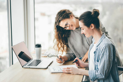 Side view of woman using laptop while standing in office