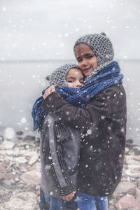 Portrait of smiling siblings embracing by lake during winter